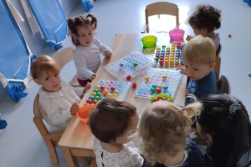 Groupe d'enfants autour d'une table manipulant des picots colorés sur des supports plastiques à la crèche Les Libellules à Vannes.