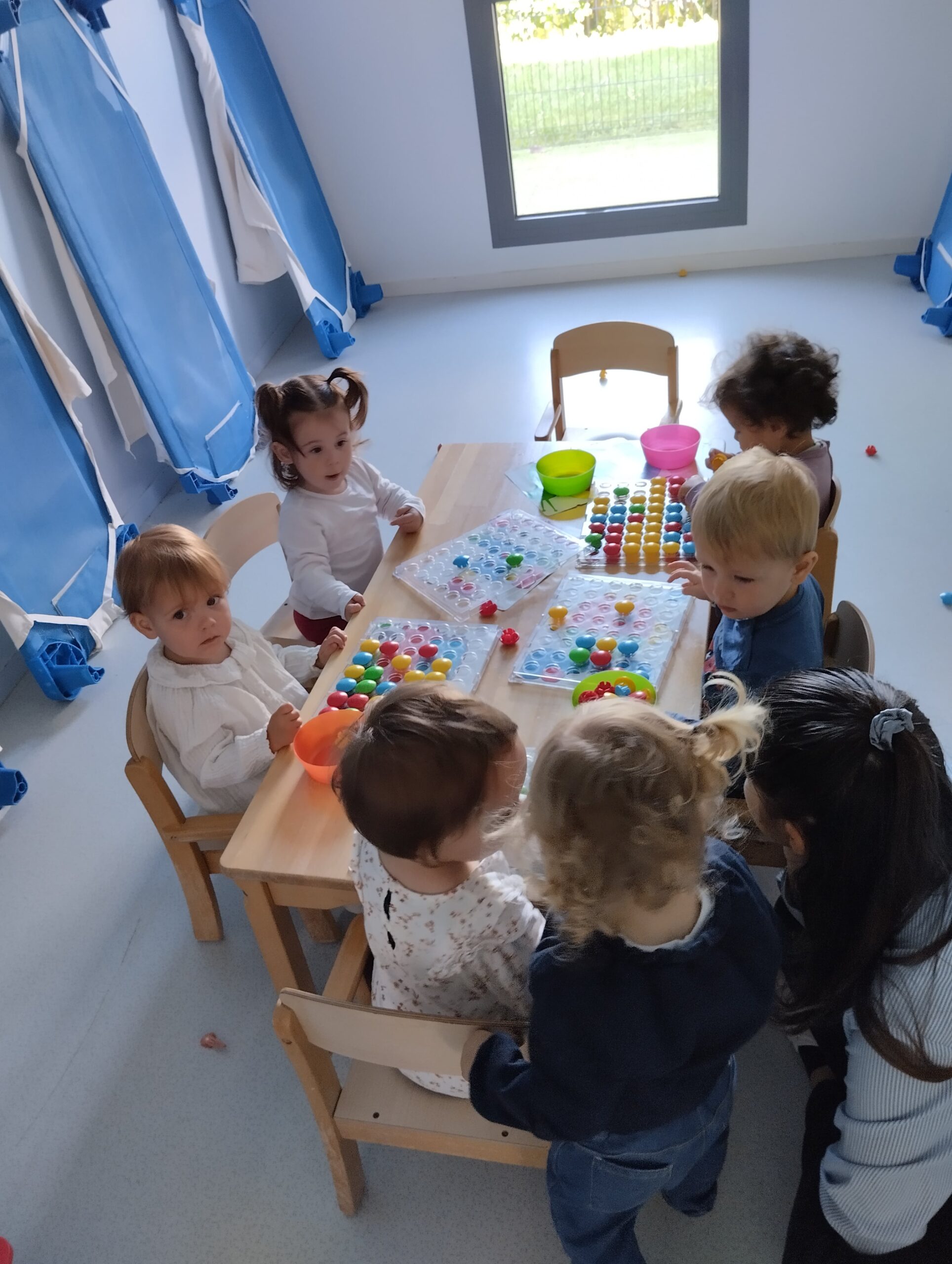 Groupe d'enfants autour d'une table manipulant des picots colorés sur des supports plastiques à la crèche Les Libellules à Vannes.