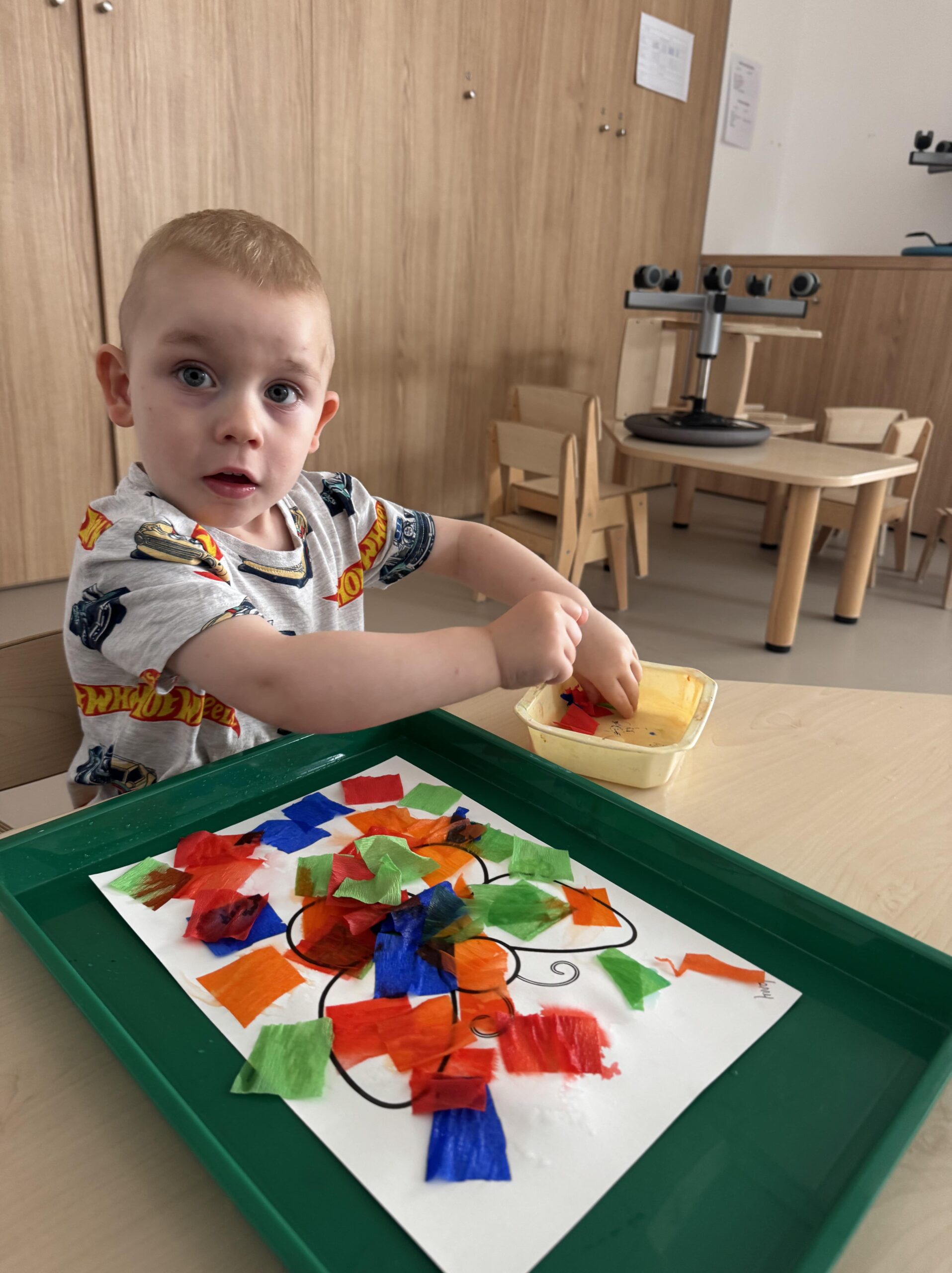 Un enfant réalise une activité de collage avec des papiers colorés à la crèche Les Papillons à Pontivy, pour stimuler sa motricité fine et sa créativité