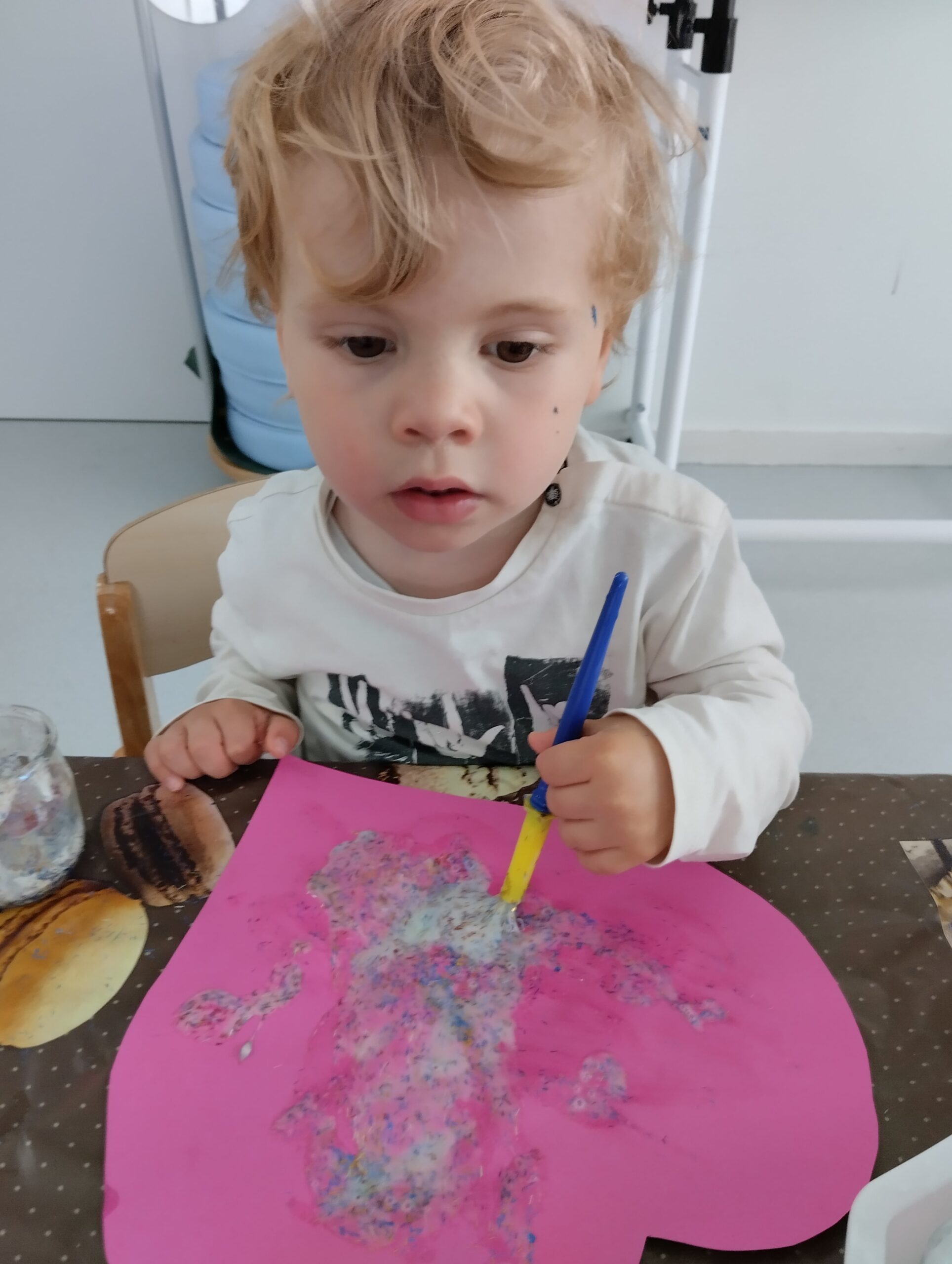 Jeune enfant concentré, en train de peindre sur une feuille rose à la crèche Les Libellules à Vannes.