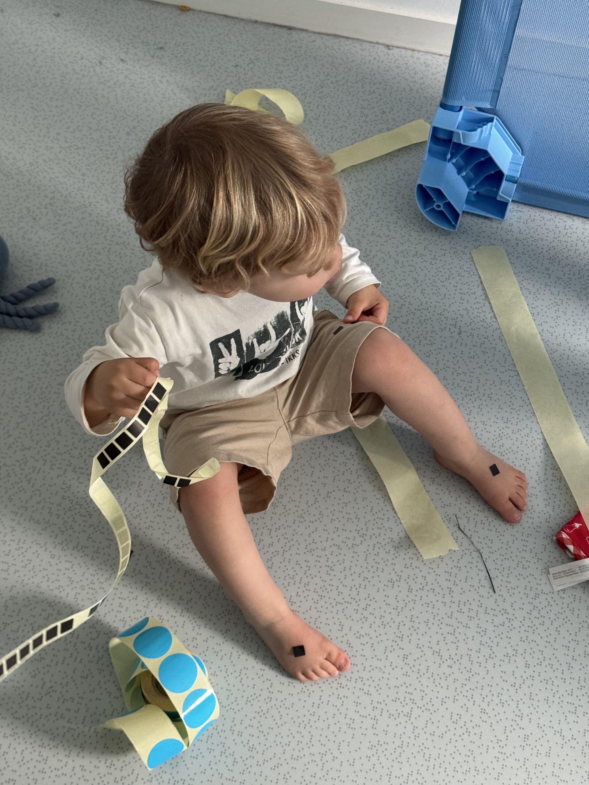 Enfant assis au sol manipulant des gommettes vertes, rouges et bleues à la crèche Les Libellules à Vannes