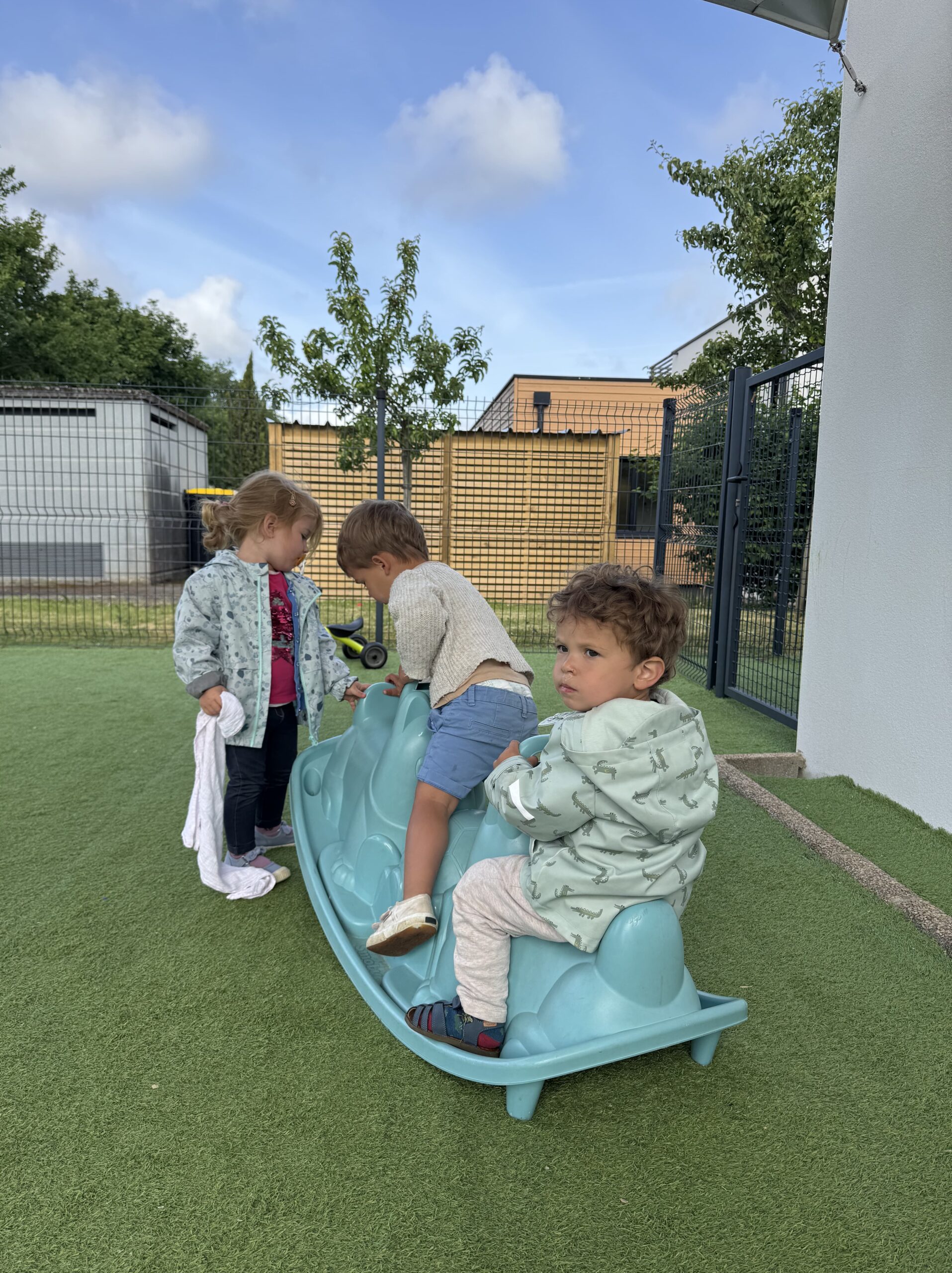 Trois enfants jouent sur une grande bascule bleue en extérieur à la crèche Les Libellules à Vannes.
