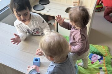 Trois jeunes enfants jouent ensemble autour d'une mini cuisine en bois dans la salle d'éveil à la crèche Les Papillons à Pontivy