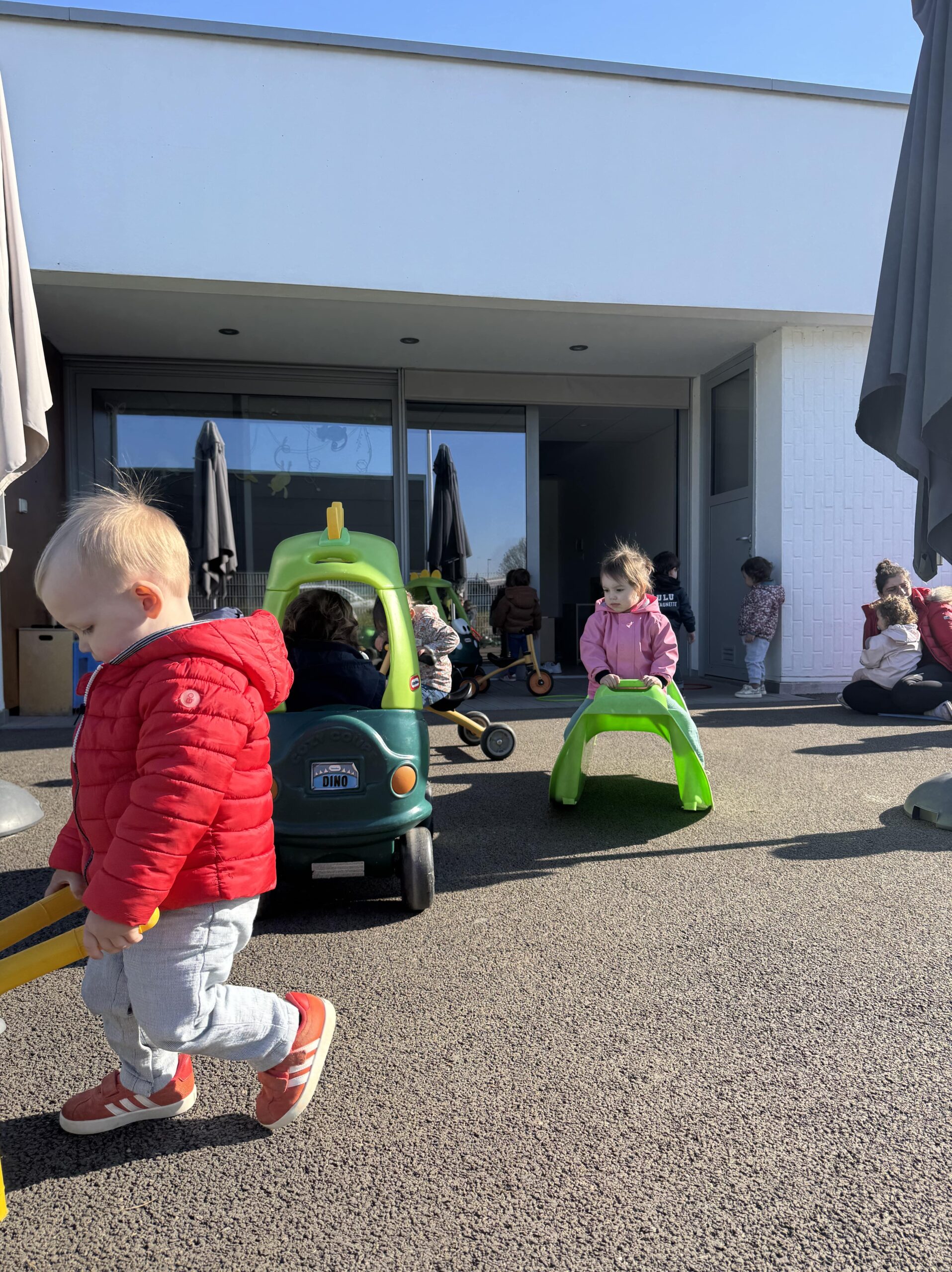 Enfants jouant librement dans la cour extérieure de la crèche Les Papillons à Pontivy, avec des porteurs en plastique.
