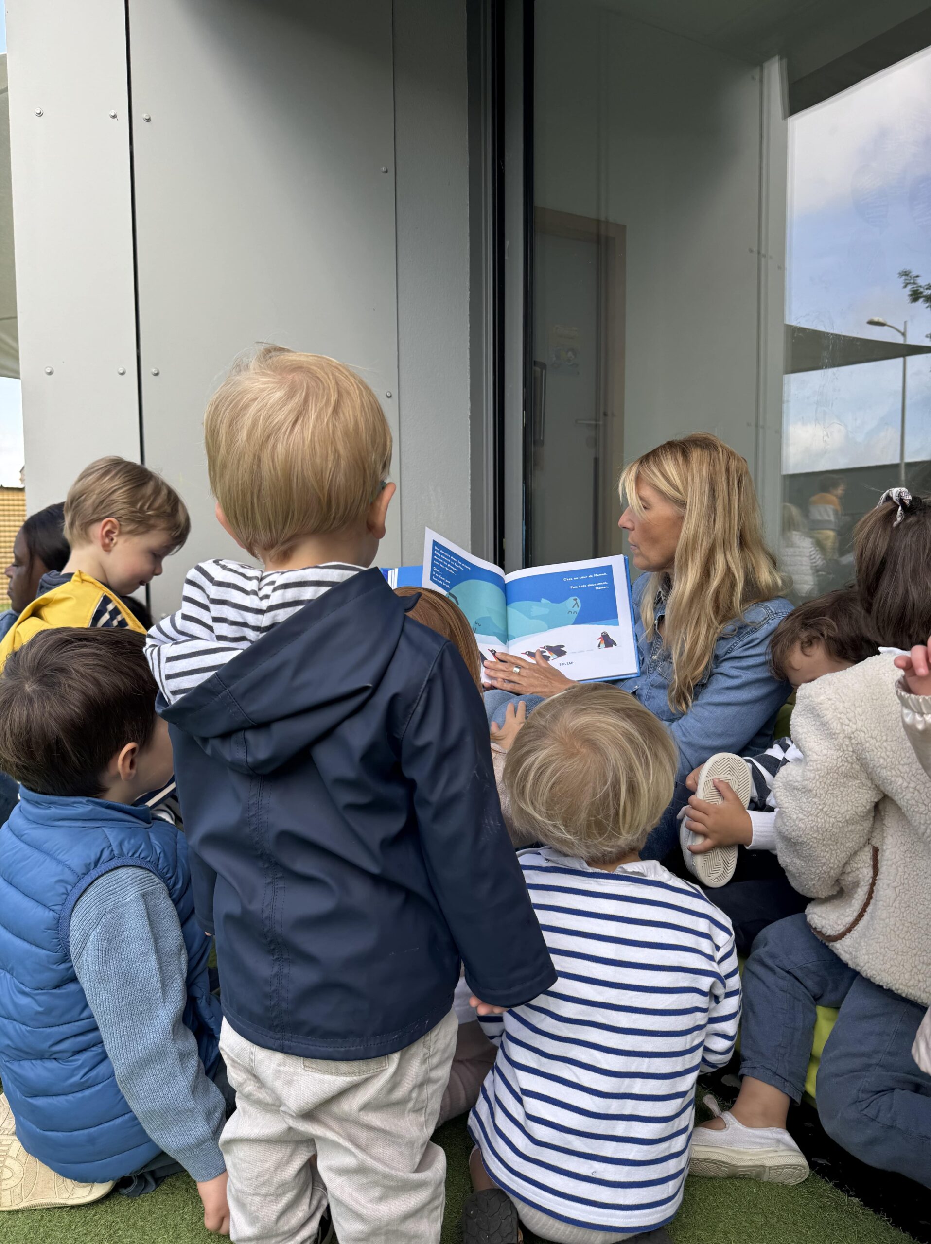 Groupe d’enfants attentifs écoutant une professionnelle lire une histoire en extérieur à la crèche Les Libellules.