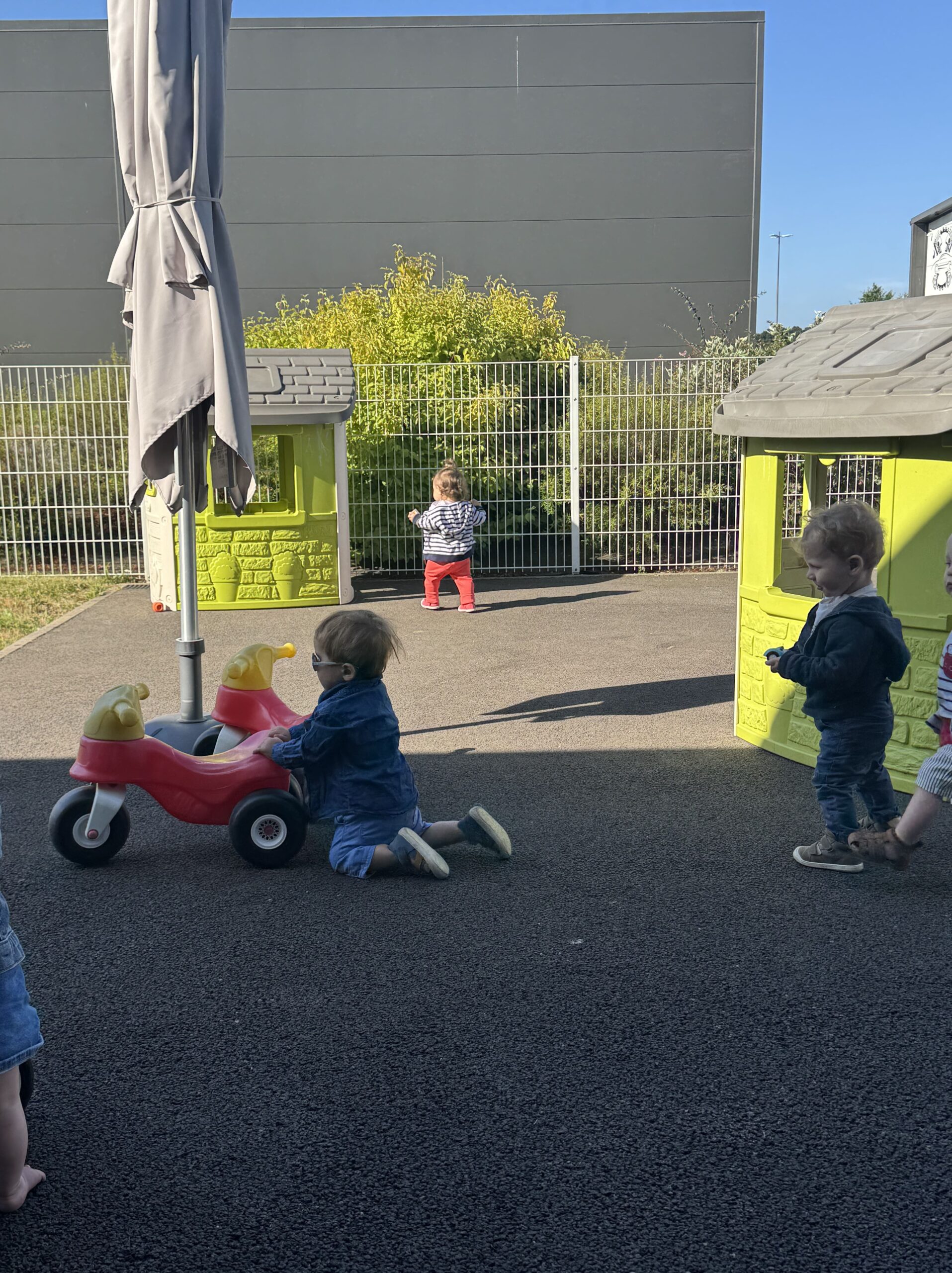 Trois jeunes enfants jouent librement dans la cour extérieur de la crèche Les Papillons à Pontivy, entre petites maisons et porteurs