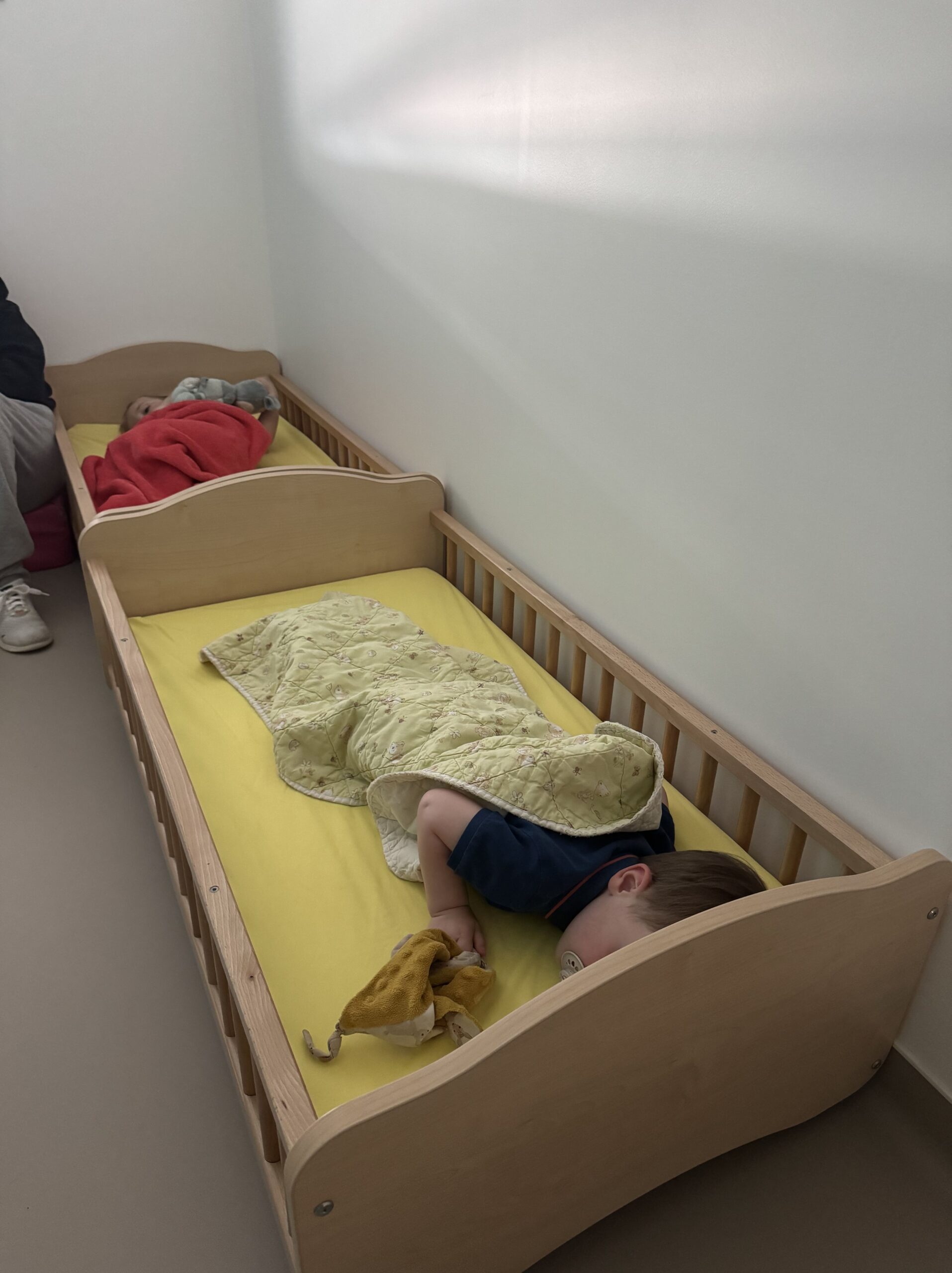 Deux enfants dorment dans des lits en bois à la crèche, chacun enveloppé dans une couverture