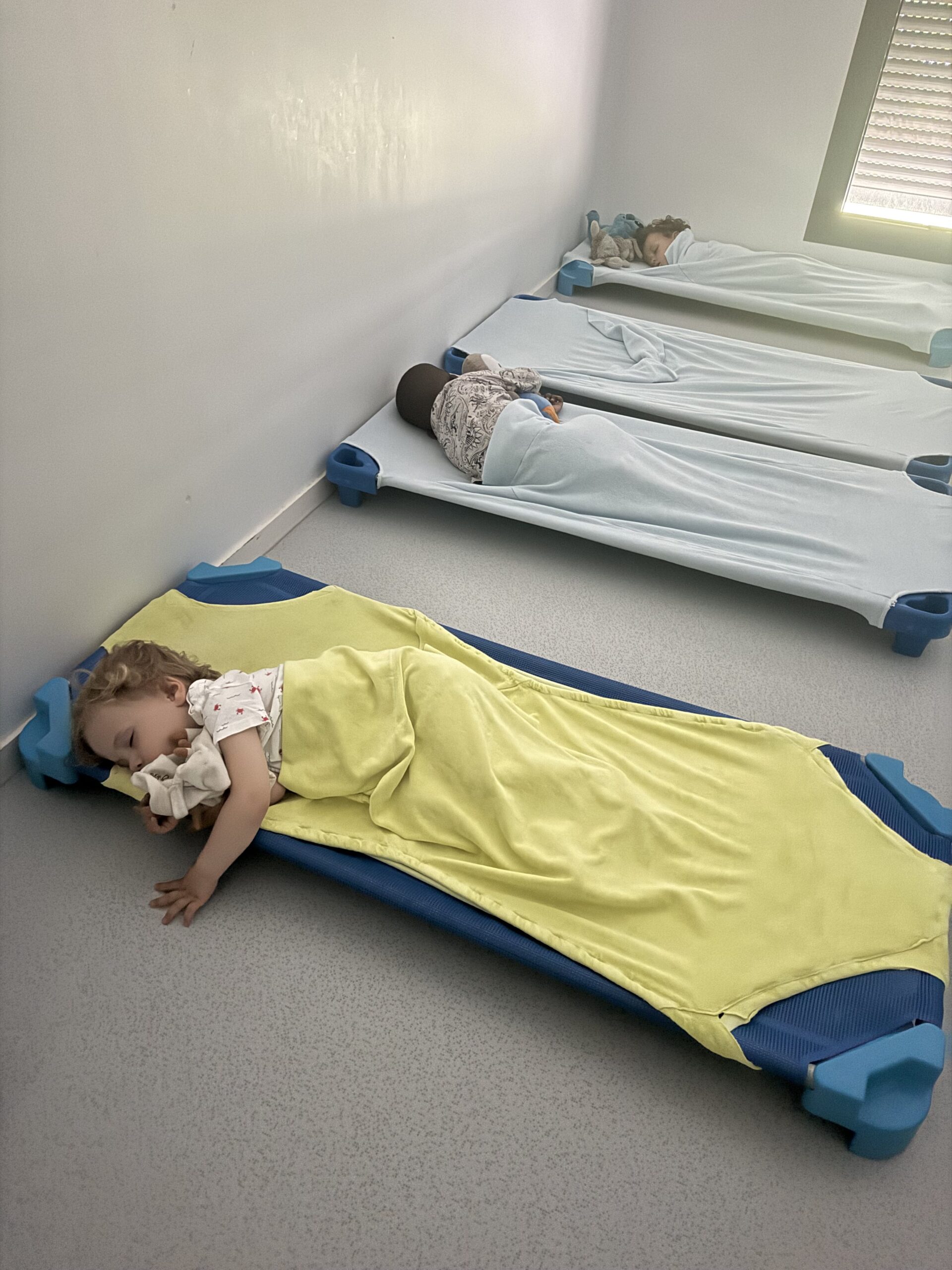 Un enfant dort paisiblement sur un lit bleu pendant la sieste à la crèche