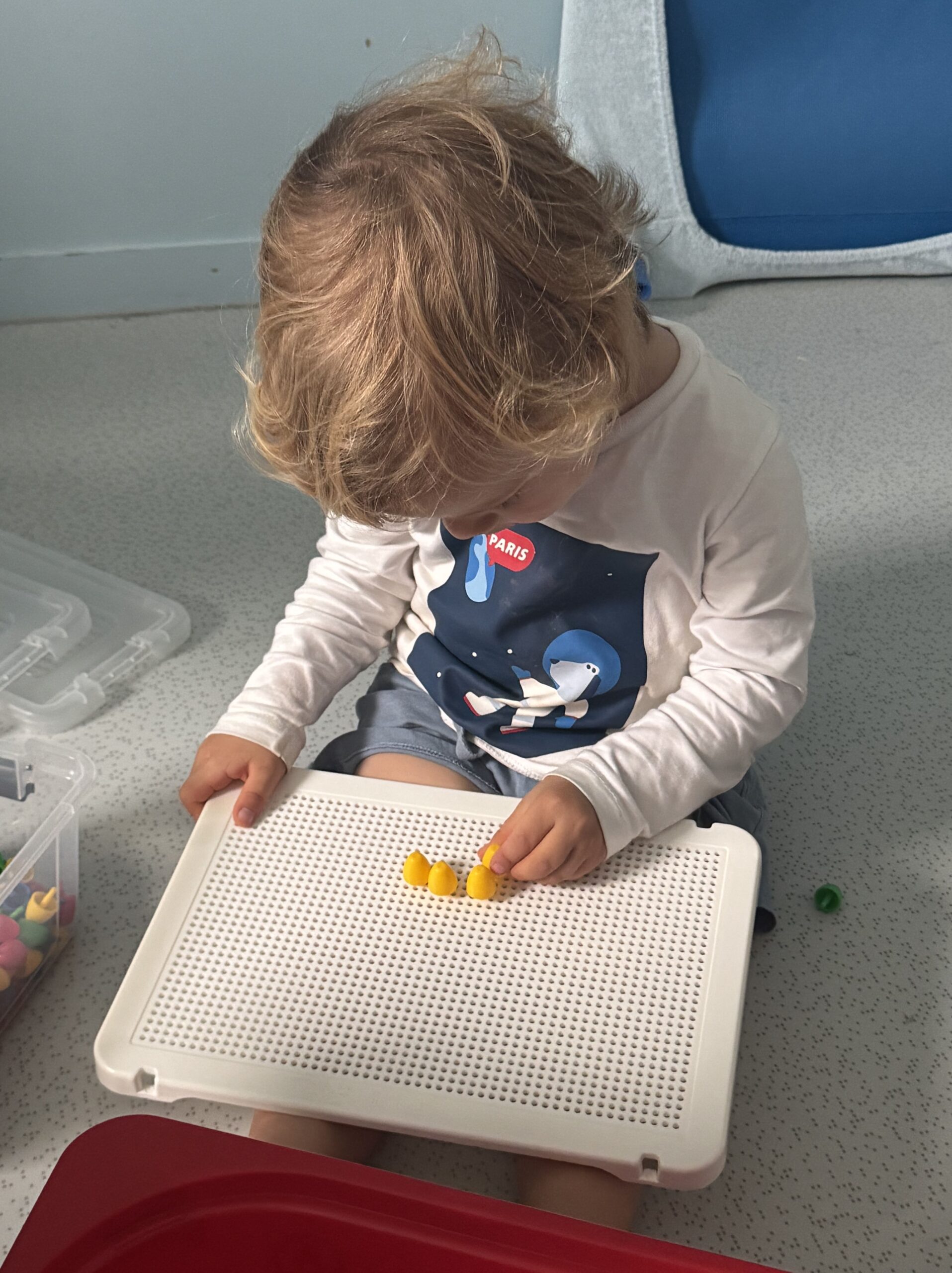 Enfant concentré, insérant des picots jaunes sur une grille de motricité fine à la crèche Les Libellules à Vannes.