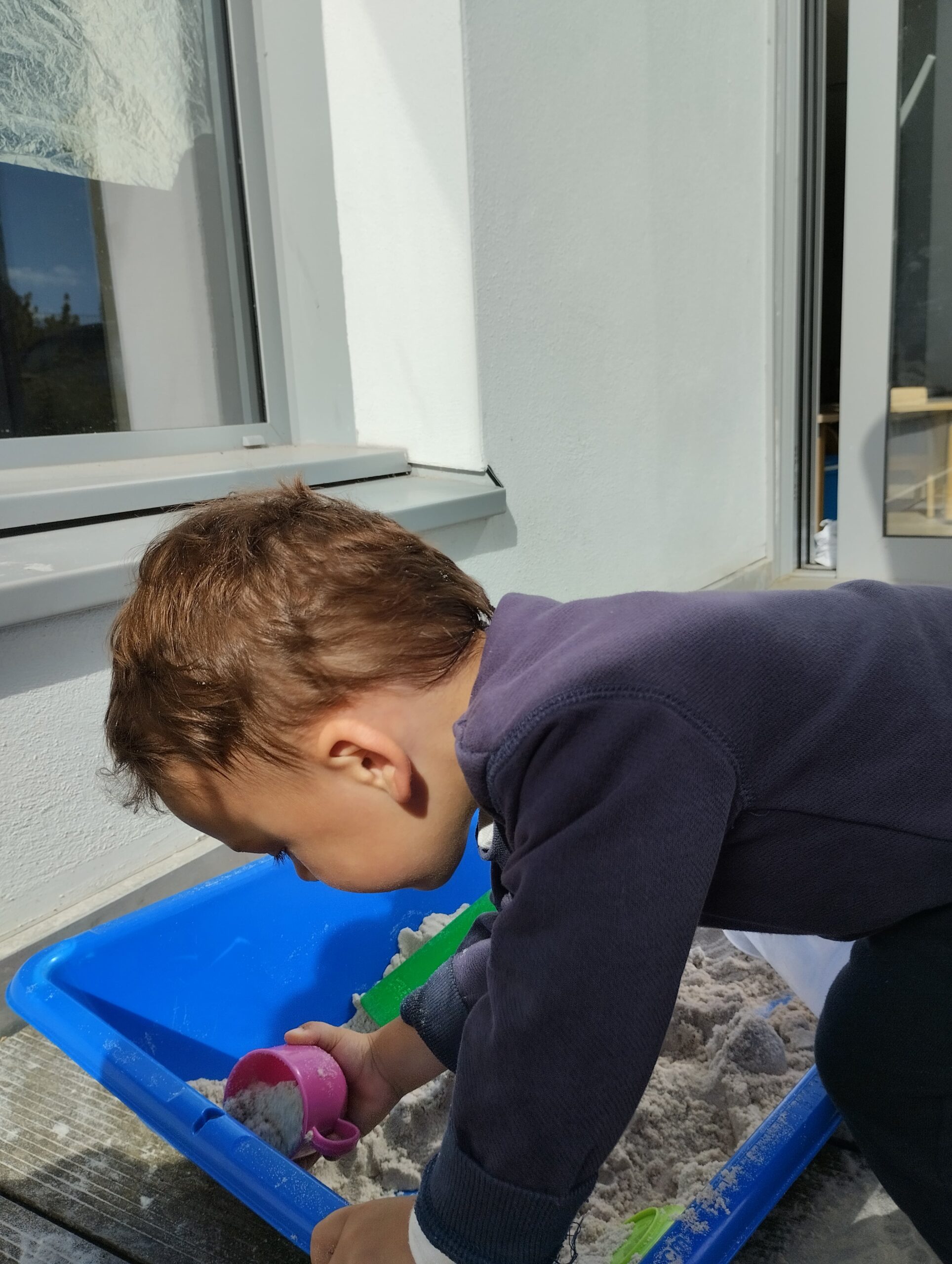 Jeune enfant penché sur un bac à sable bleu à la crèche Les Papillons de Pontivy.