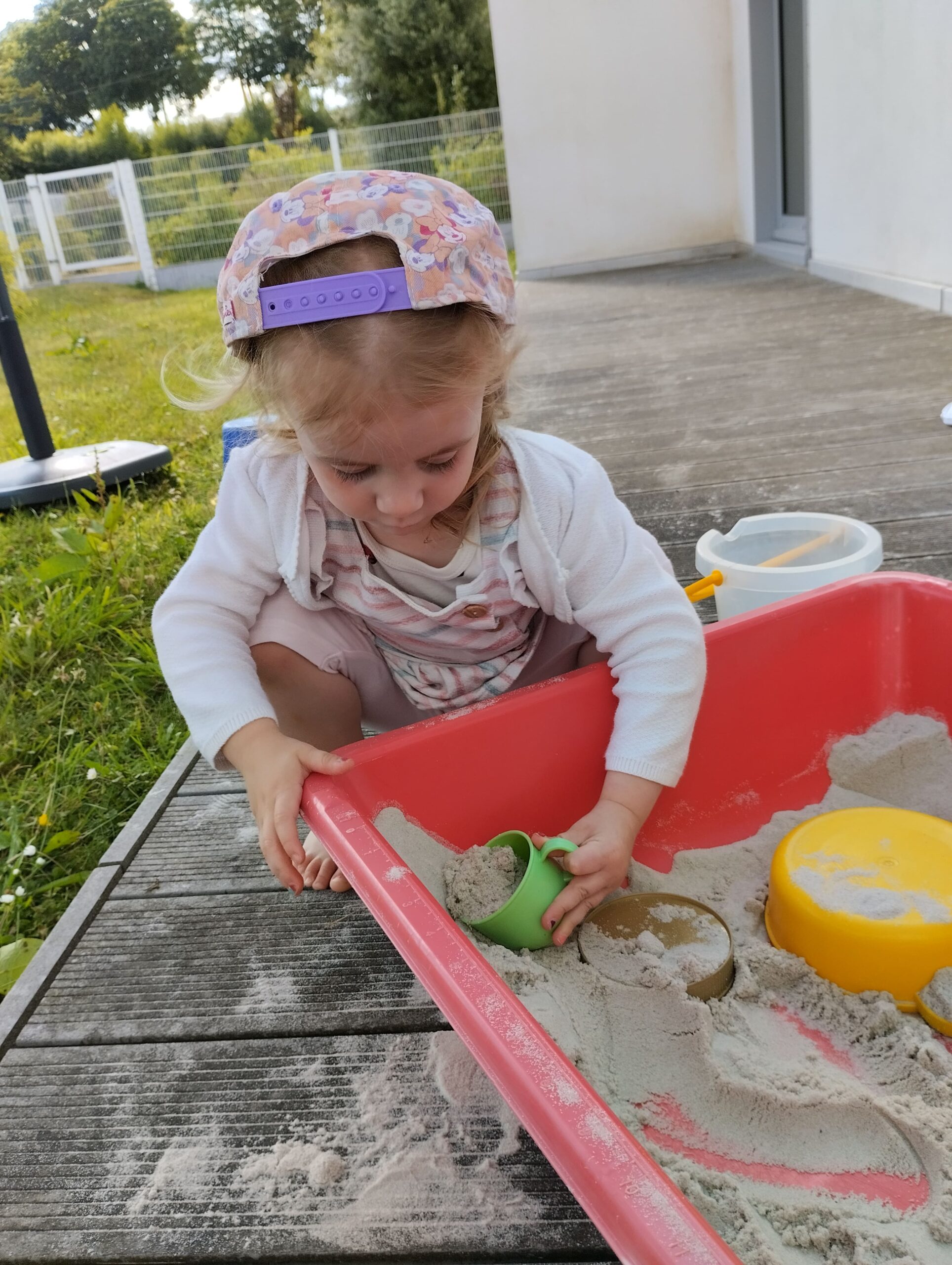 Petite fille avec casquette à fleurs jouant au sable à la crèche Les Papillons de Pontivy.