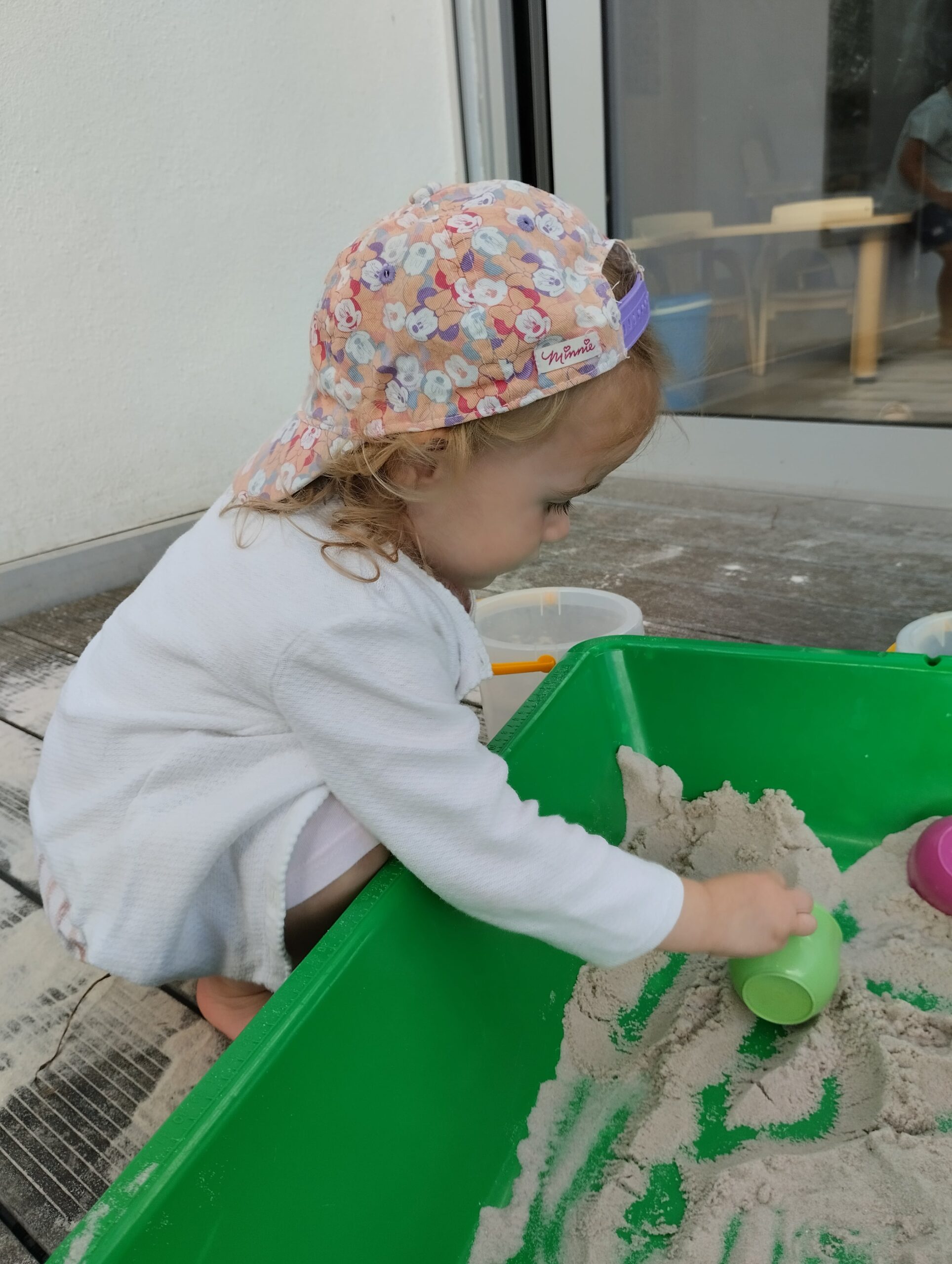 Petite fille concentrée dans un bac à sable vert à la crèche Les Papillons de Pontivy.