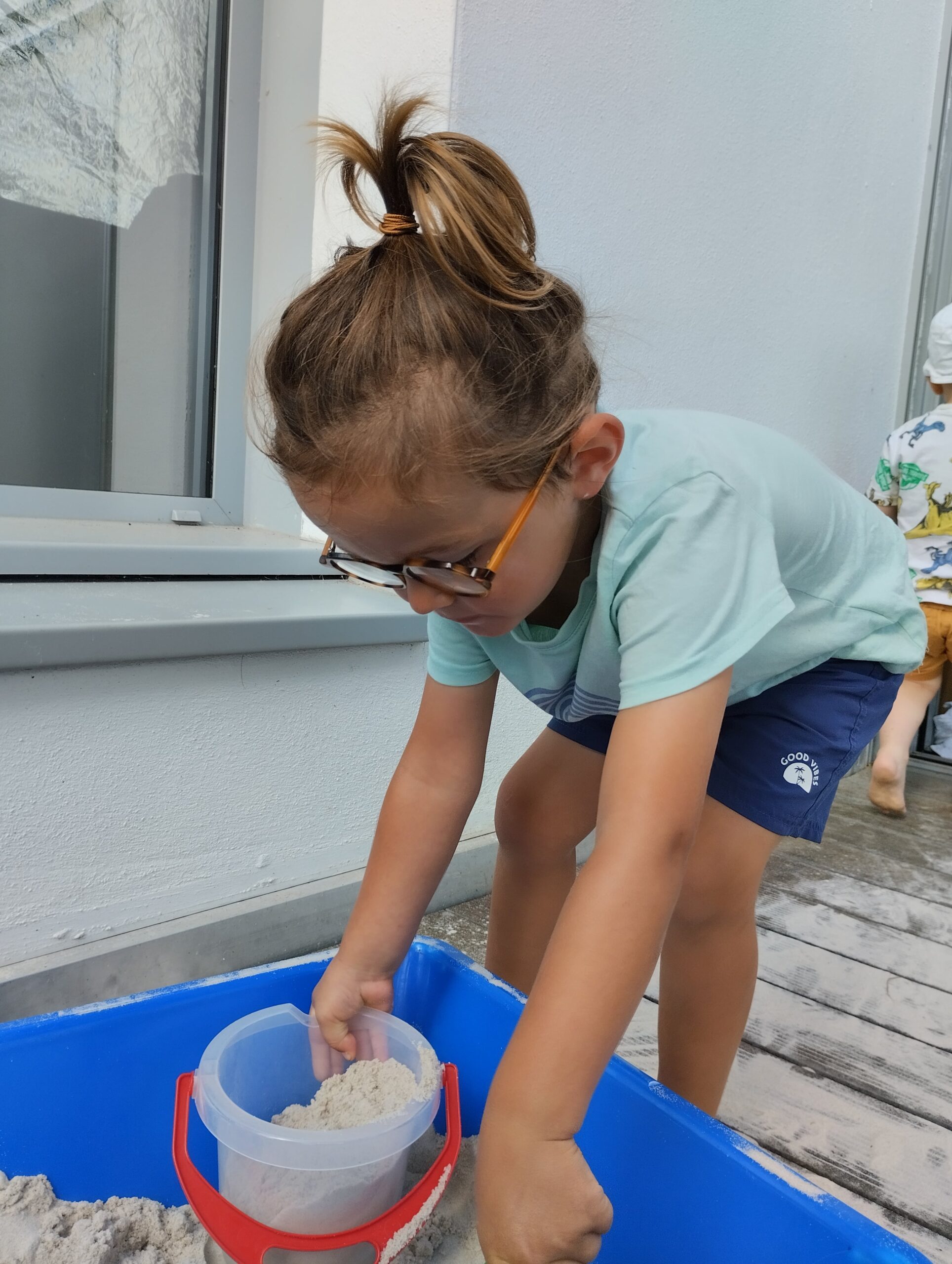 Petit garçon avec lunettes jouant dans un bac à sable à la crèche Les Papillons à Pontivy.