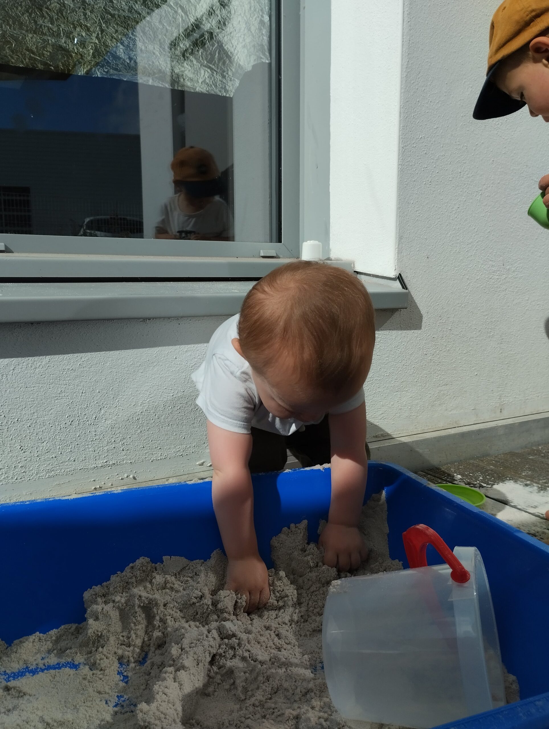 Bébé penché dans un bac bleu, les mains dans le sable à la crèche Les Papillons à Pontivy.