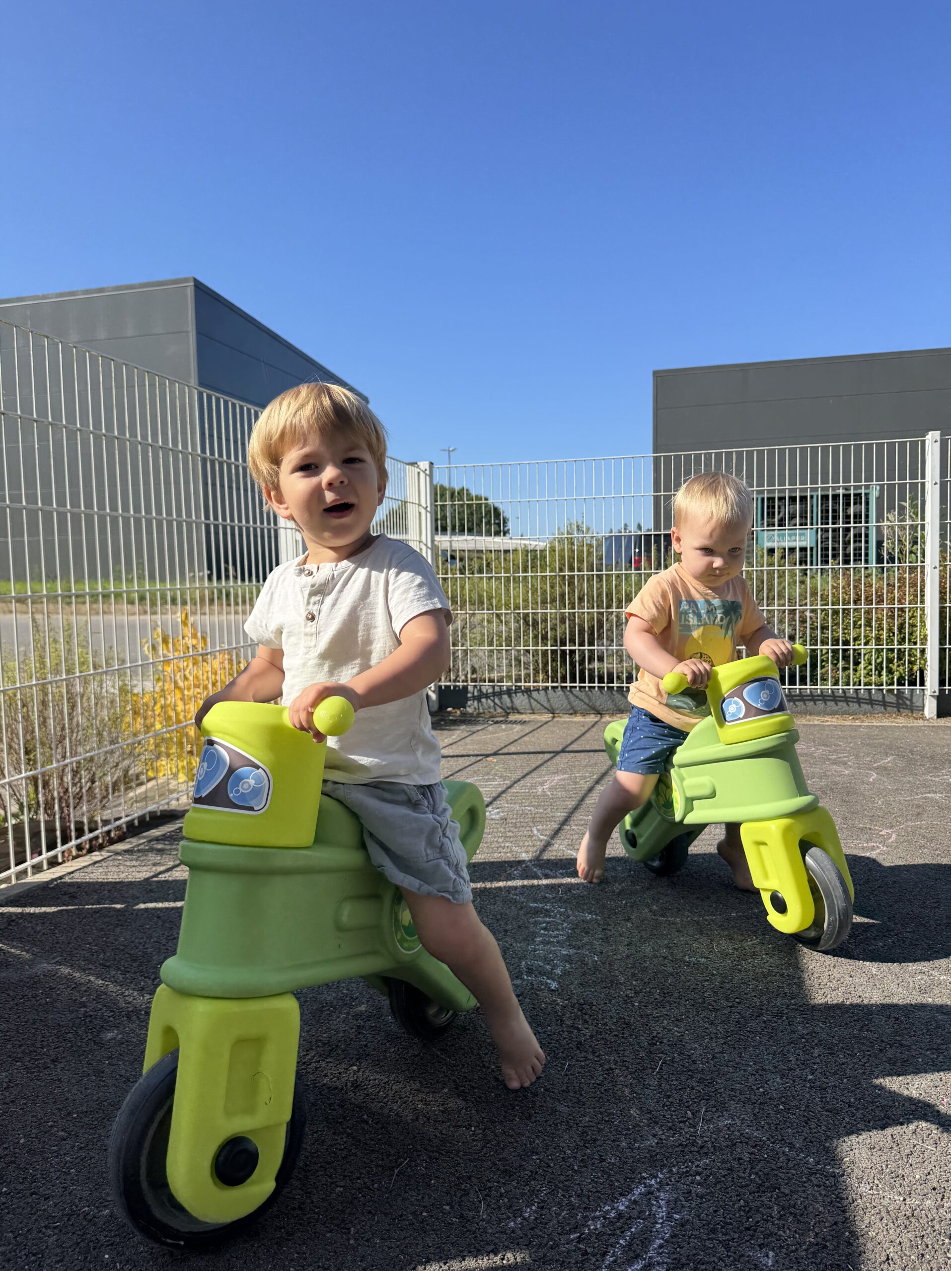Deux enfants sur des draisiennes vertes s’amusent en extérieur à la crèche Les Papillons