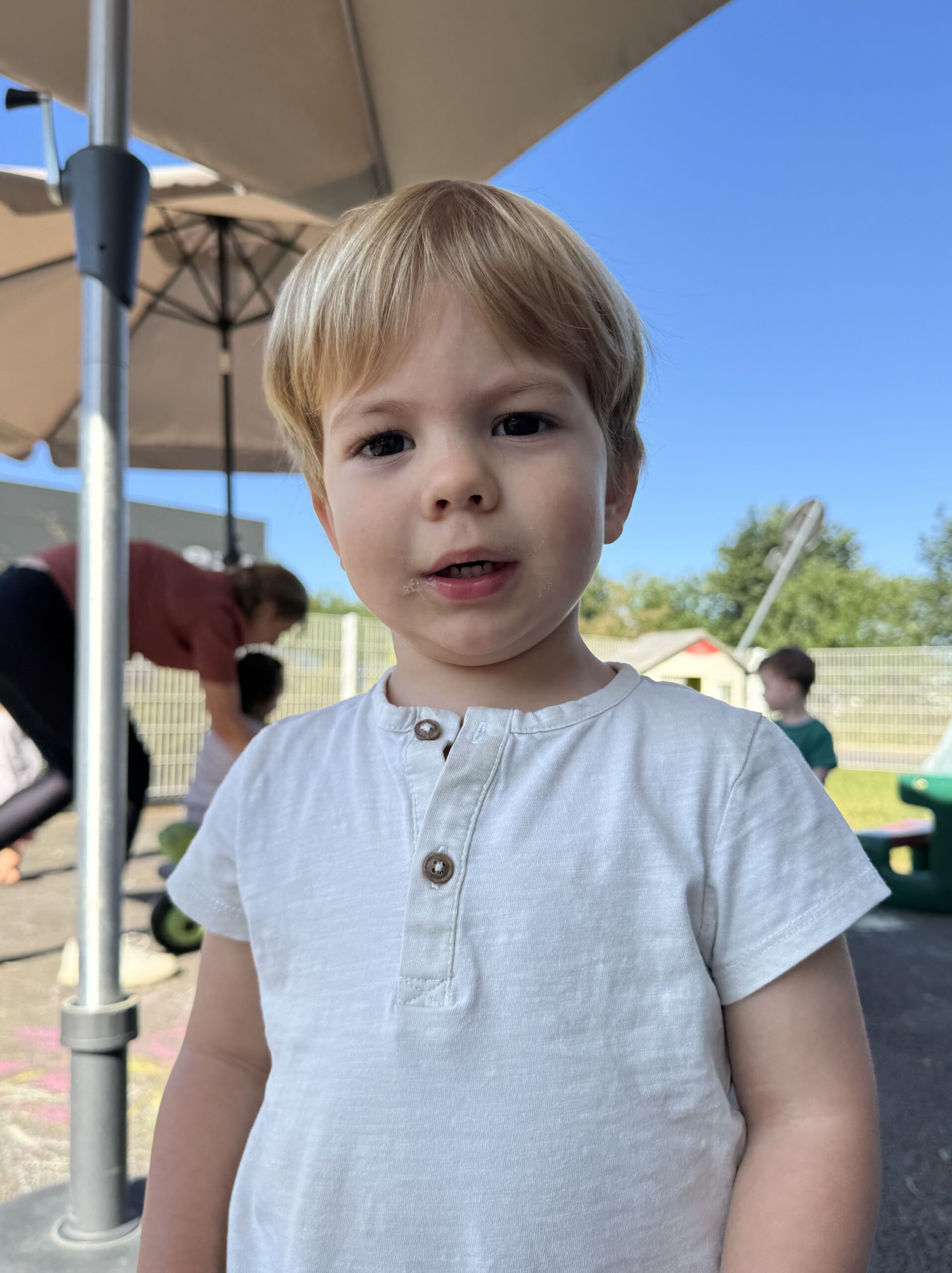 Enfant blond, souriant dans la cour de la crèche Les Papillons, sous le soleil d'été