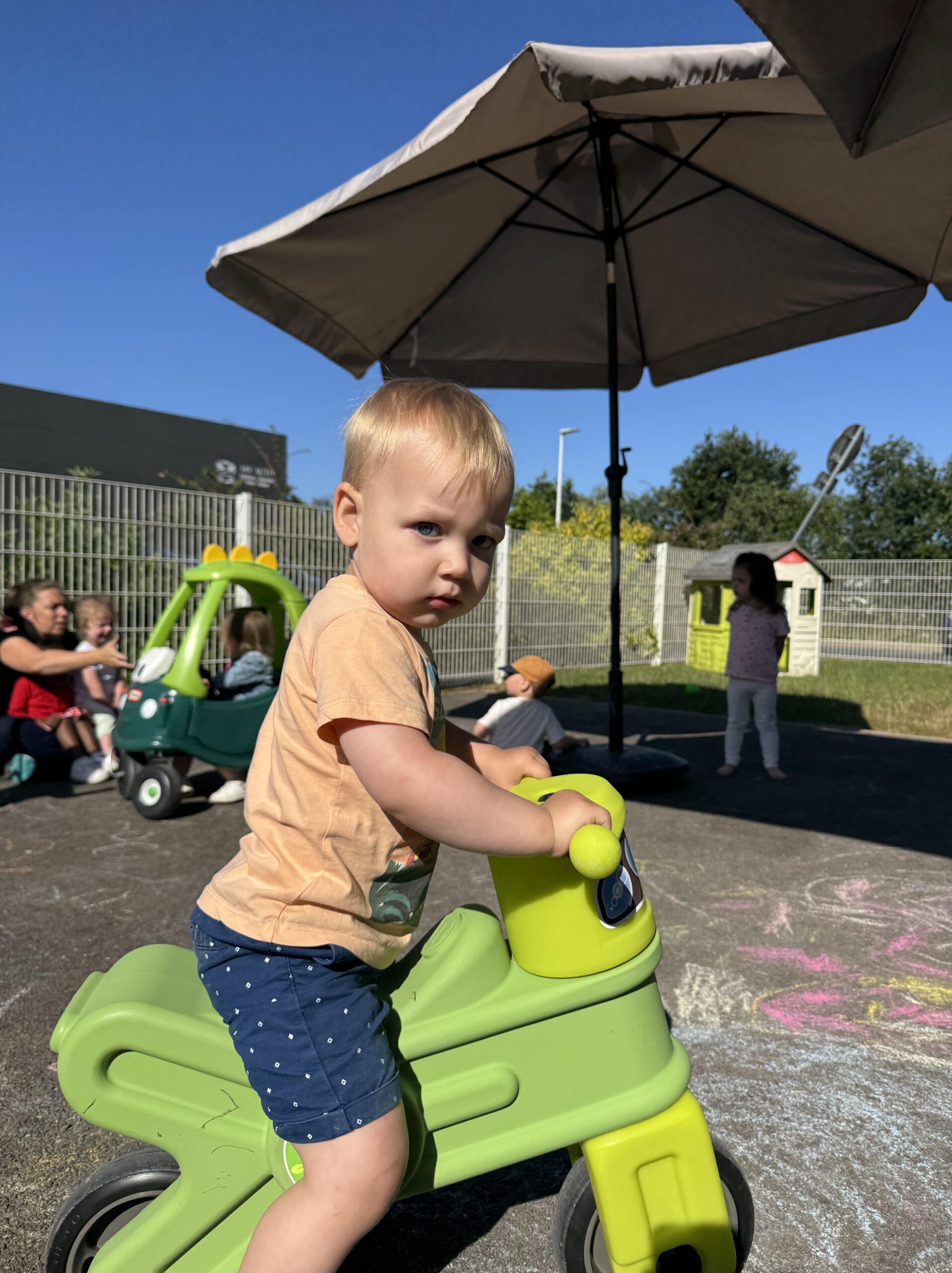 Enfant sur une draisienne verte dans la cour de la crèche Les Papillons.