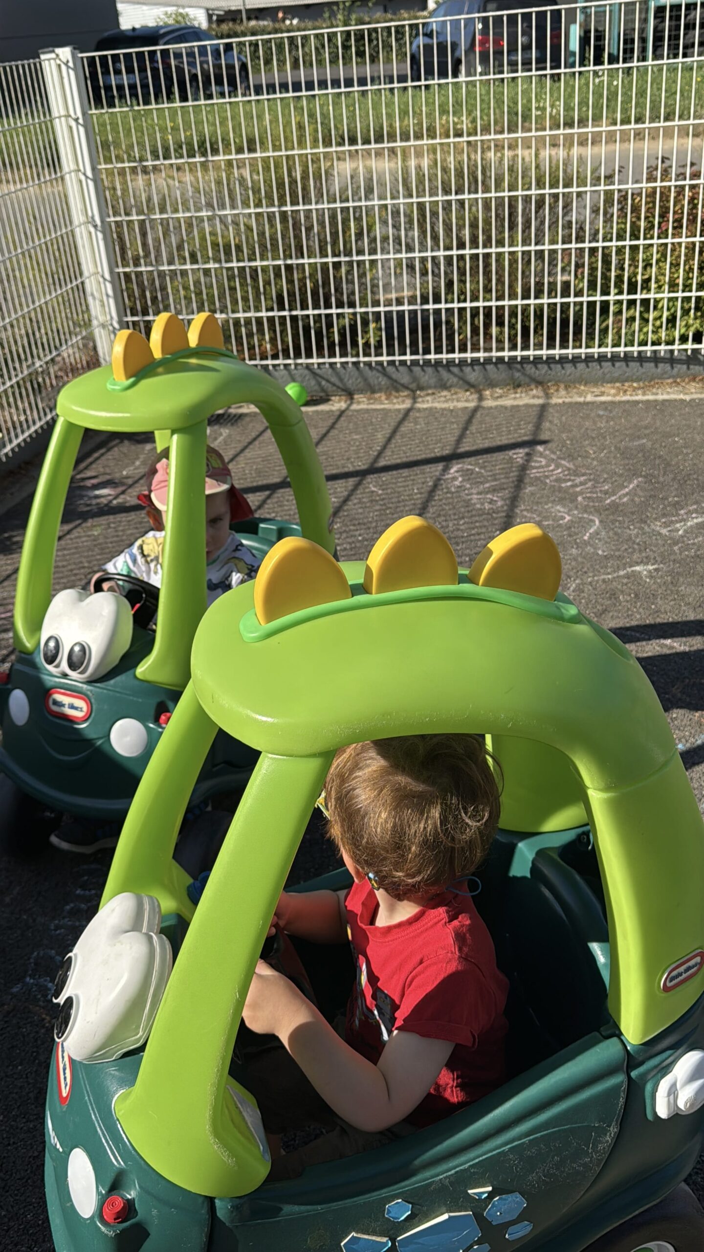 Deux enfants dans des petites voitures vertes s'amusent dans la cour de la crèche Les Papillons