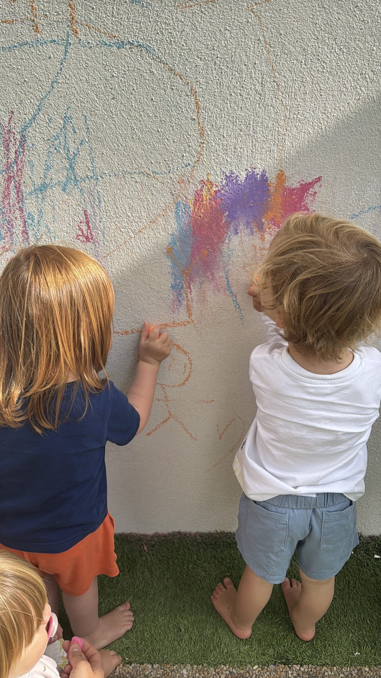 Deux enfants dessinent côte à côte sur un mur avec des craies multicolores à la crèche Les Libellules à Vannes.