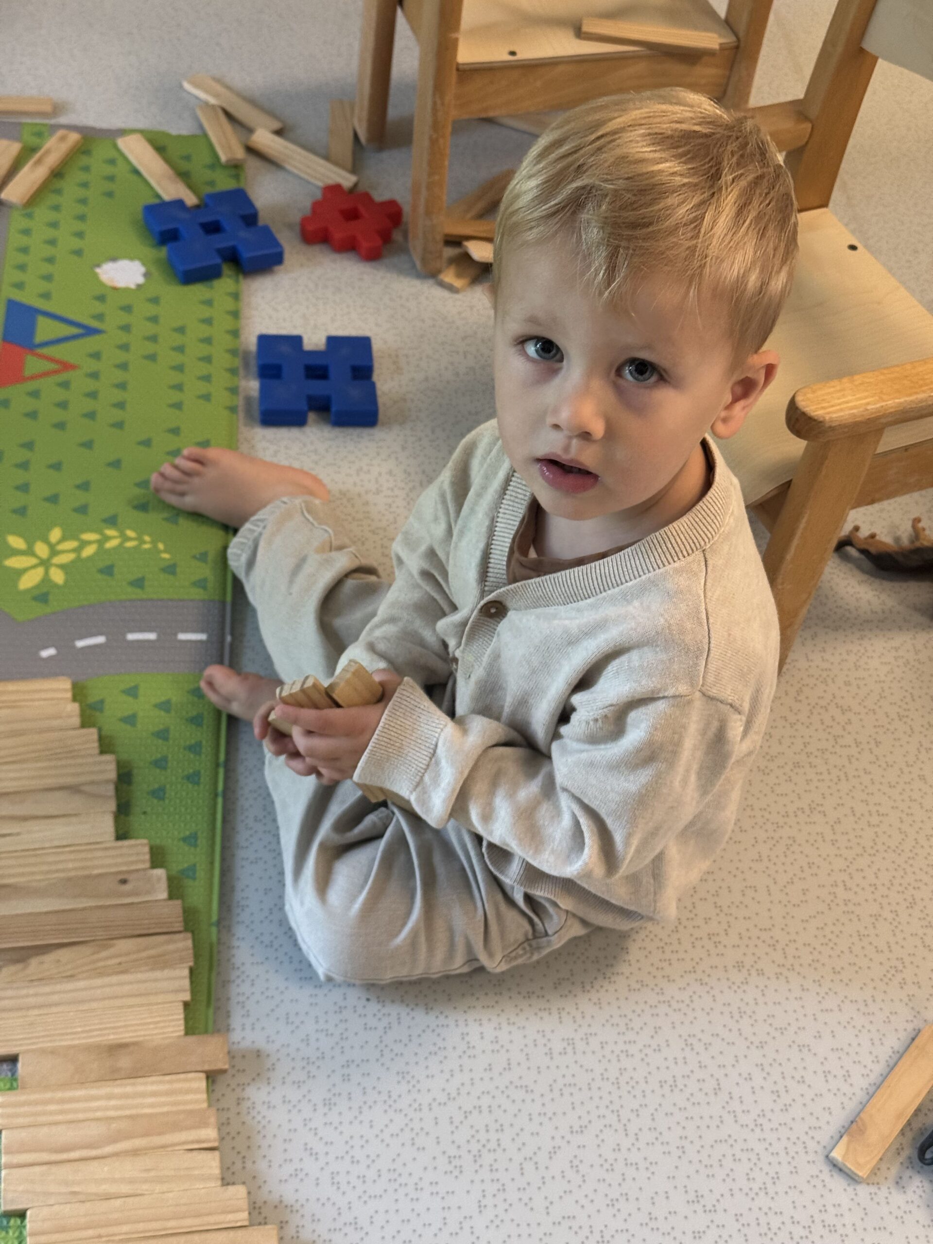 Enfant blond assis par terre construisant avec des planchettes de bois à la crèche Les Libellules à Vannes