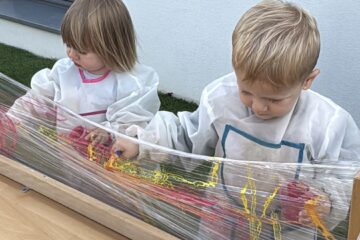 Deux enfants en blouse de peinture décorent un film plastique tendu avec des pinceaux et de la peinture vive à la crèche Les Libellules de Vannes