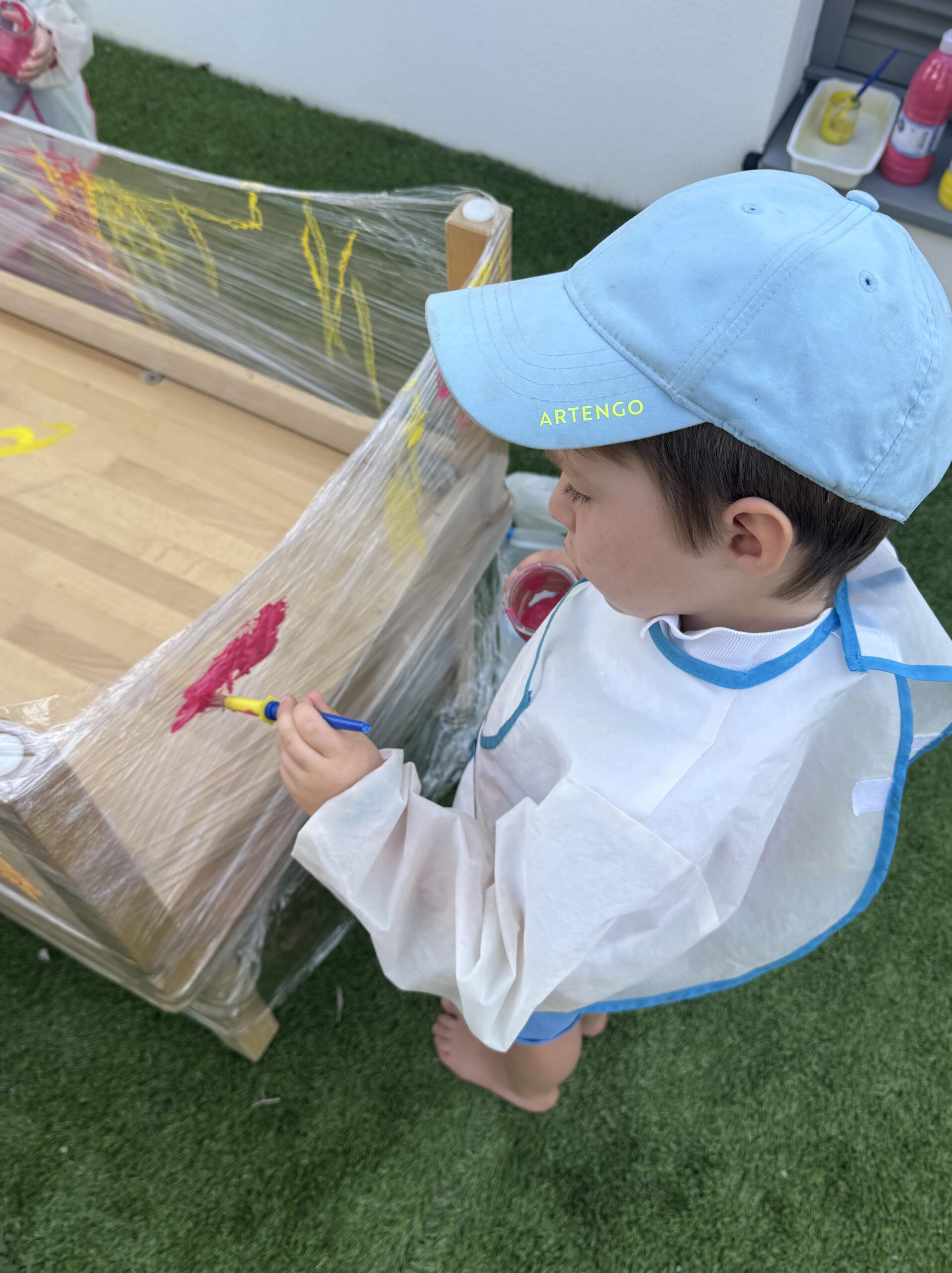 Petit garçon en casquette bleue participant à une activité de peinture en extérieur à la crèche Les Libellules à Vannes